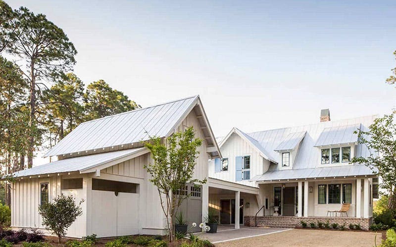 A white house with a metal roof and a paved driveway leading up to it.