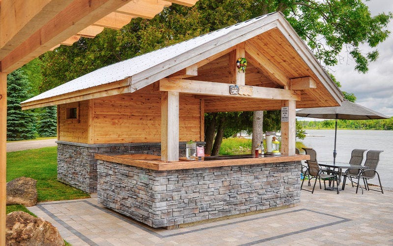 A compact outdoor kitchen featuring a bar area, surrounded by greenery and designed for al fresco dining.