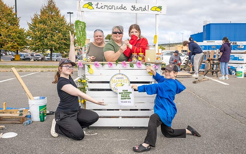 KENT Building Supplies associate and family members pose beside a lemonade stand during a lively community gathering.