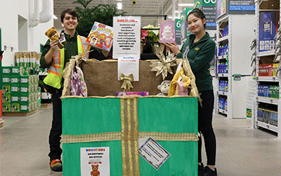 Deux associés de magasin aident les clients avec une boîte de jouets, mettant en évidence le soutien communautaire et les cadeaux dans un cadre dynamique de magasin