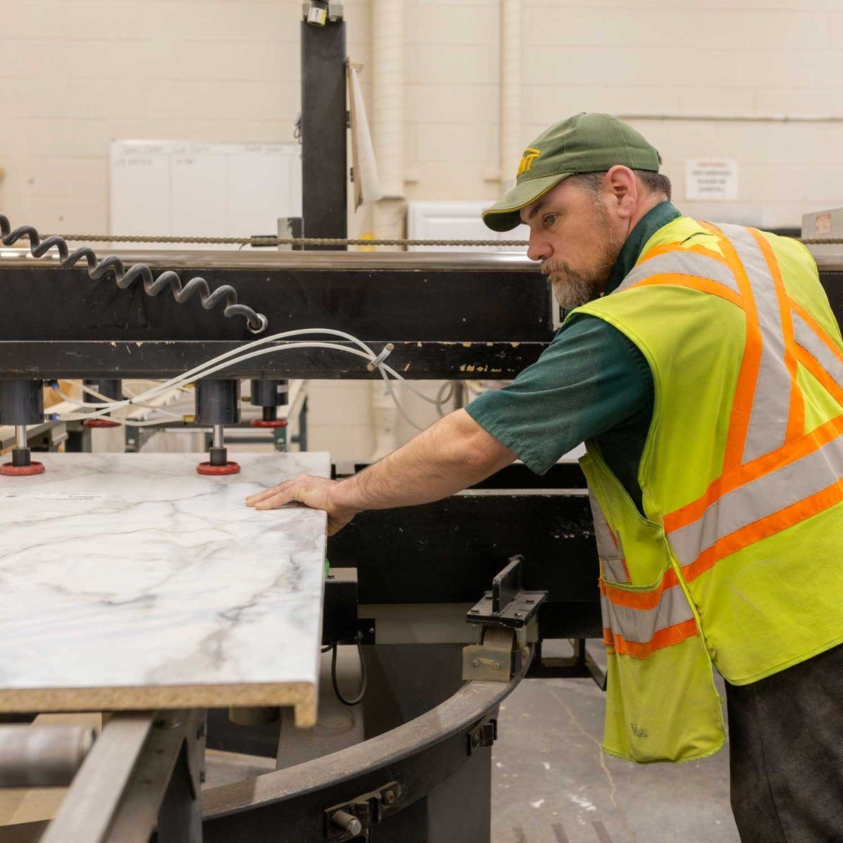 Worker operating a cutting machine to trim a countertop slab in a workshop setting with safety gear image